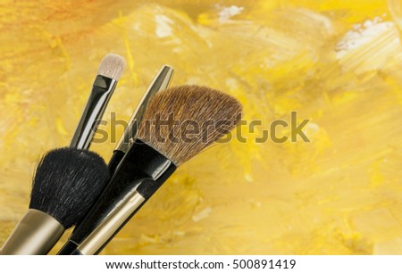 Makeup brushes on a blurred golden yellow background. A horizontal template for a makeup artist's business card or flyer design, with copyspace