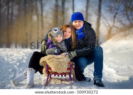 the happy close-knit family poses on the sledge in the winter wood