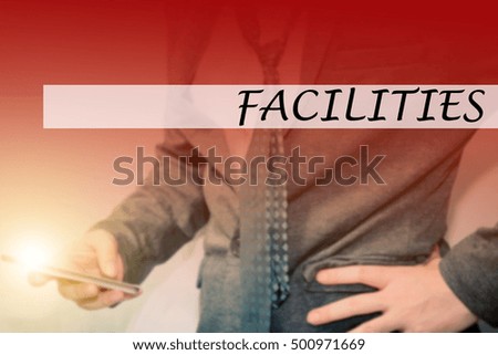 Hand writing FACILITIES with the young business man on background. Business concept. Stock Photo.