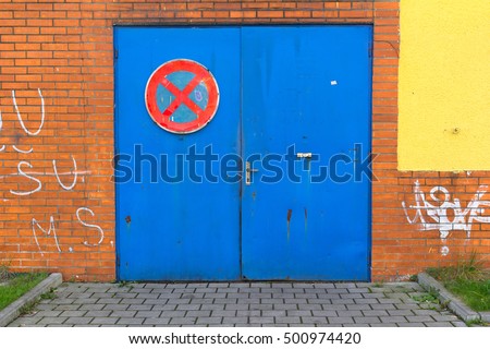 Detail of building with old blue door. Traffic sign of caution to not park in front of doors.