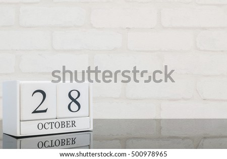 Closeup white wooden calendar with black 28 october word on black glass table and white brick wall textured background with copy space , selective focus at the calendar