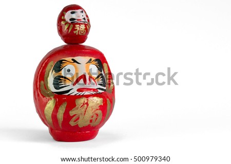 Two red Daruma dolls, a small one on top of a bigger one, with the typical missing eye,  standing on the left of the picture, facing to the right, on a white background.