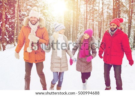 love, relationship, season, friendship and people concept - group of smiling men and women walking ad having fun in winter forest