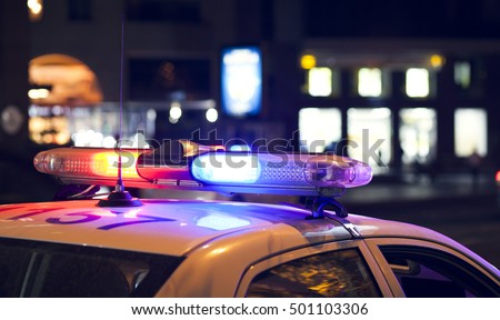 Blue light flasher atop of a police car. City lights on the background.