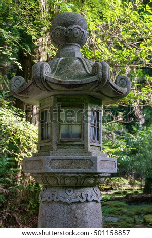 Japanese stone lantern, spirit house surrounded by trees with lush green leaves