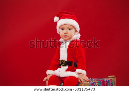 Beautiful little baby celebrates Christmas. New Year's holidays red background