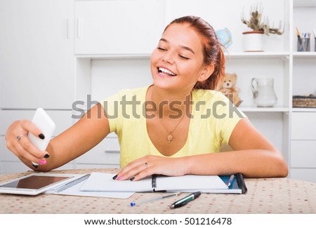 smiling teenager girl doing selfie during homework at the table
