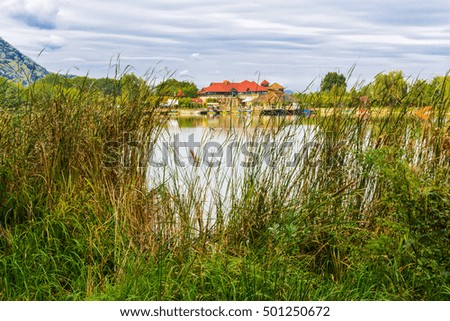 Houses on the shore of the lake. Mountain lake for fishing against the background of green vegetation, blue morning sky in cirrus clouds and the rising sun. Early morning. Western Ukraine.