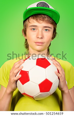 Studio portrait of a boy teenager with football over green background.