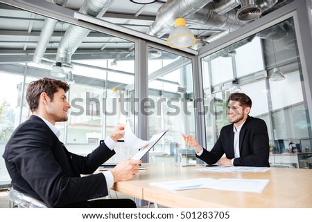 Two cheerful young businessmen creating business plan on meeting in office