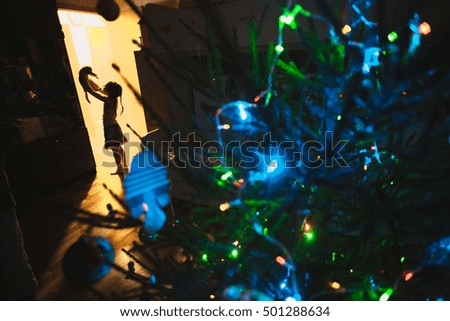 Little girl with her kitten standing behind christmas tree with the light silhouette at night