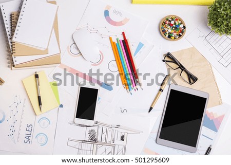 Top view of messy office workplace with financial reports, empty electronic devices, supplies and other items. Mock up