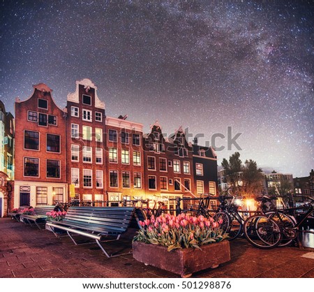 Fantastic starry sky at night in Amsterdam. Beautiful illumination of buildings near the water in the channel. Art photography