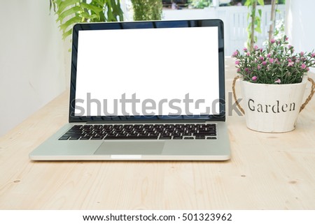 Office table with blank screen on laptop and rose flower on pot at tree garden background, Working at home concept. View form front office desk.