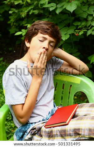 boy with book yawning close up photo in the summer garden. Boy yawn.