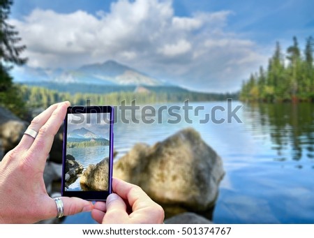 View over the mobile phone display during taking a picture of landscape in nature. Holding the mobile phone in hands and taking a photo. Focused on mobile phone screen. 