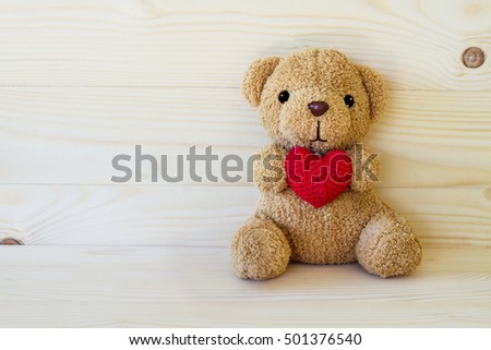 Teddy bear holding a heart-shaped pillow on wood board background