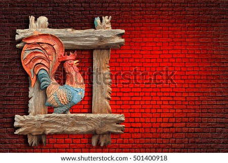 Red fiery rooster in the wooden window frame. Symbol Eastern 2017 new year. Red brick wall background with light spot. Copy space