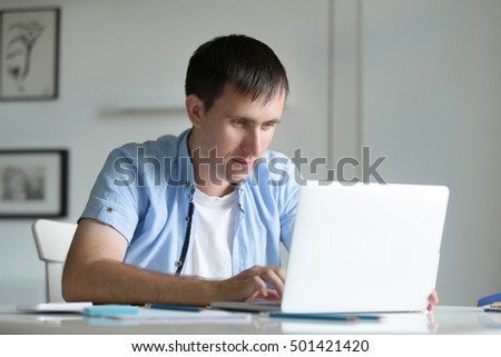 Portrait of a young man working at the desk with a laptop, looking at the screen, education, business concept photo
