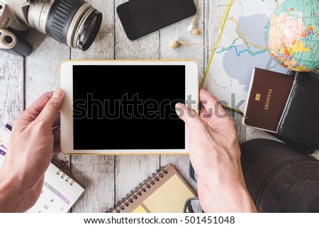 Top view of Male hands holding tablet with travel equipment on white wooden table background