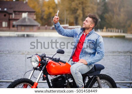 trendy guy in the denim jacket and the motorcycle makes a selfie