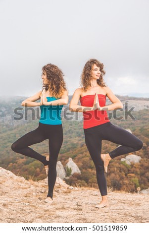 Couple of young pretty women are doing stretching fitness exercise over breathtaking view of mountains