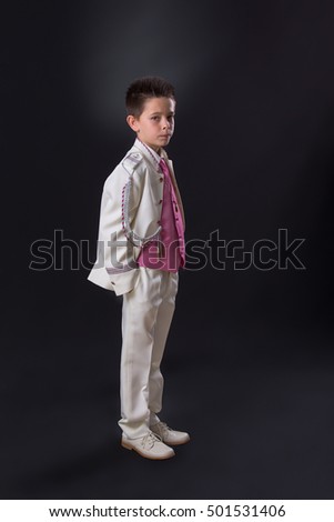 Young boy in his First Holy Communion looking at camera and standing with a serious expression on a black background.