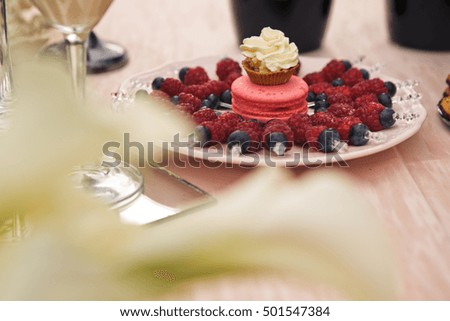 Pink macaroon stand on the plate full of berries