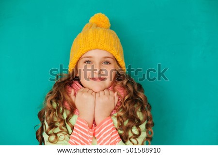 Cute little lady wearing yellow woolen cap and warm scarf against turquoise background
