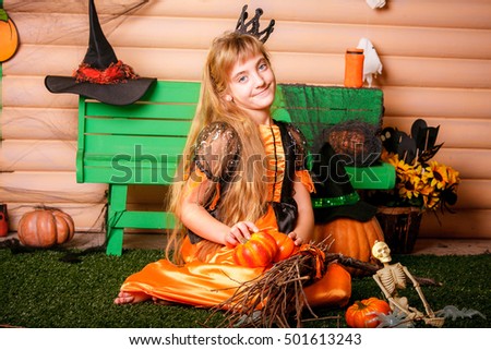 Happy Halloween! Cute cheerful little witch with a book of spells. Beautiful child girl in witch costume sitting on grass,  laughing.