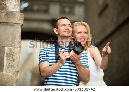 Positive man and woman tourists taking camera in hands and photographing in city