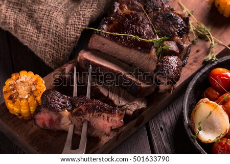Grilled Steak sliced on a cutting board. Meat with Grilled Vegetables. Wooden background.