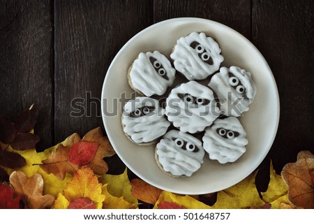 Funny scary mummy cookies for Halloween on autumn leaves background, selective focus