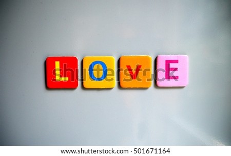 Photo of four colorful toy magnets with letters on refrigerator door, making the word Love. Toy magnets with English alphabet letters on a refrigerator. Love word.