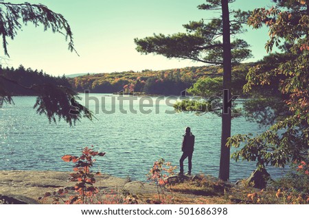 Silhouette of a nature photographer standing on a cliff in the sunset light admiring  the North South lake in the Catskill mountains. Vintage processed. Travel, adventure, outdoors and fashion concept