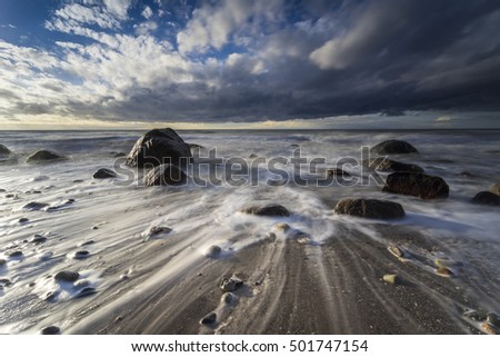 Baltic Sea at nightly light and long exposure, Undergoing sun irradiates the sea and stones in the sea water, Moving lake and foaming waves on the shore,