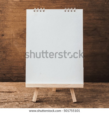 wooden easel with white paper on wooden background