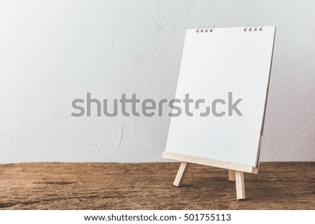 wooden easel with white paper on wooden background