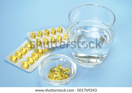 Fish oil omega 3 capsules and glass water on blue table
