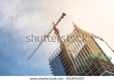 Working crane and safety net on a modern office and residential building under construction against blue sky in Hanoi, Vietnam. Green grid prevent objects falling from height. Industrial Background.