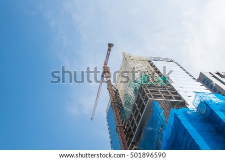 Working crane and safety net on a modern office and residential building under construction against blue sky in Hanoi, Vietnam. Green grid prevent objects falling from height. Industrial Background.