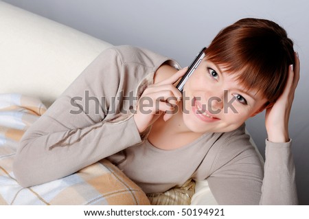 Young charming brunette in a gray jacket resting on the sofa and on the phone