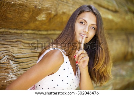 Young beautiful brunette woman has put forefinger to lips as sign of silence, against green summer garden
