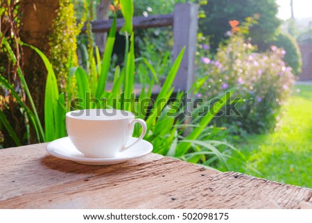 a selective focus picture of a cup of coffee on wooden table in green garden 