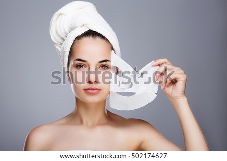 Girl with almost rended white mask. Model pulling away mask from her face. Hair wrapped with towel. Head and shoulders, studio, indoors Royalty-Free Stock Photo #502174627