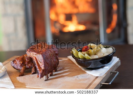 Closeup of baked pork chops with vegetables. Served on a wooden cutting board. In the background of a burning fireplace completes the unique atmosphere.