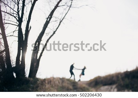 Blurred background. The girl and the guy circling, holding hands, standing on the horizon next to a tree, as small silhouettes. Concept of love, family and happy walk.
