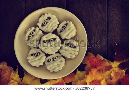 Funny scary mummy cookies for Halloween on autumn leaves background, selective focus, toned