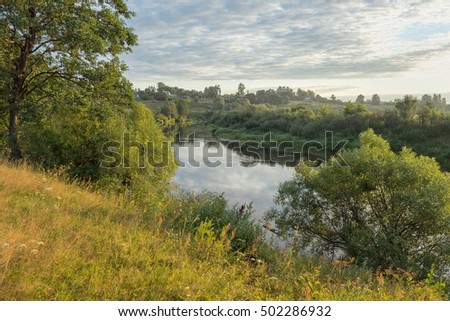 View on sunny river valley with wooden houses on bank at sunset. Bulatovo village, Kaluzhskaya region, Russia.
