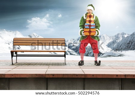 Young elf in christmas clothes on train station and winter landscape of Alps 